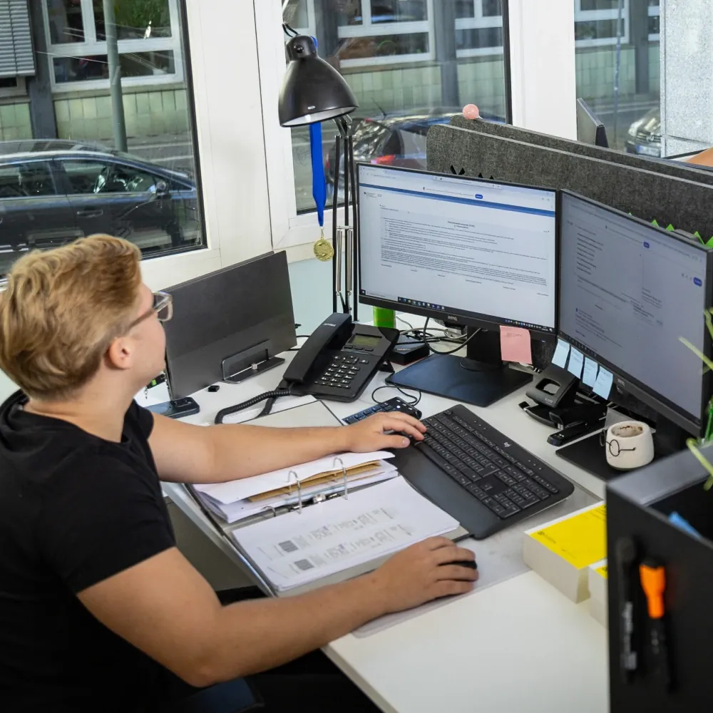 Mitarbeiter bei H+ am Schreibtisch, Hände auf Tastatur und Maus