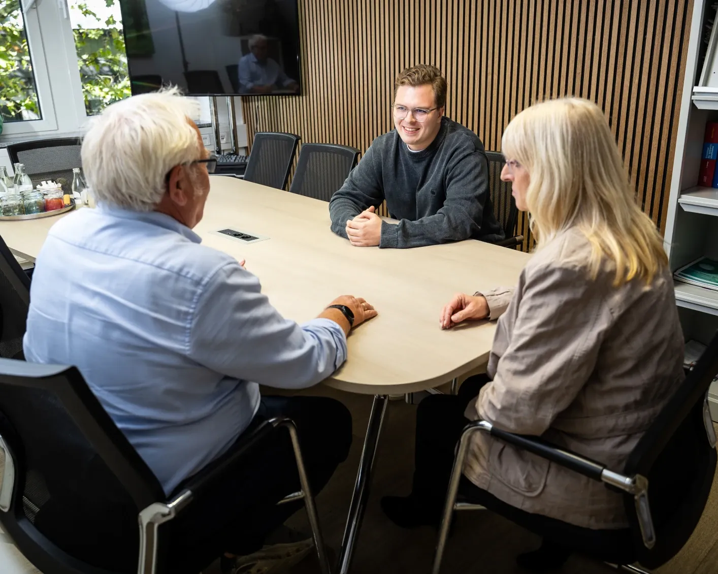 Tim im Beratungsgespräch mit zwei Mandanten am Besprechungstisch
