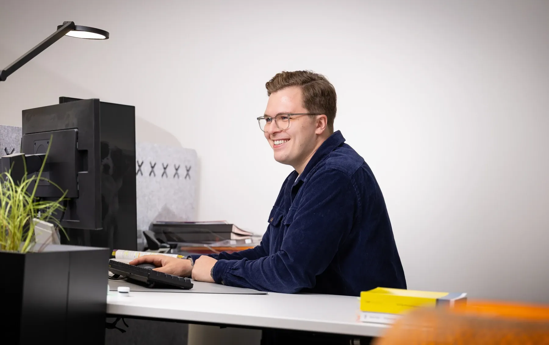 Tim lächelnd an seinem Arbeitsplatz im Büro